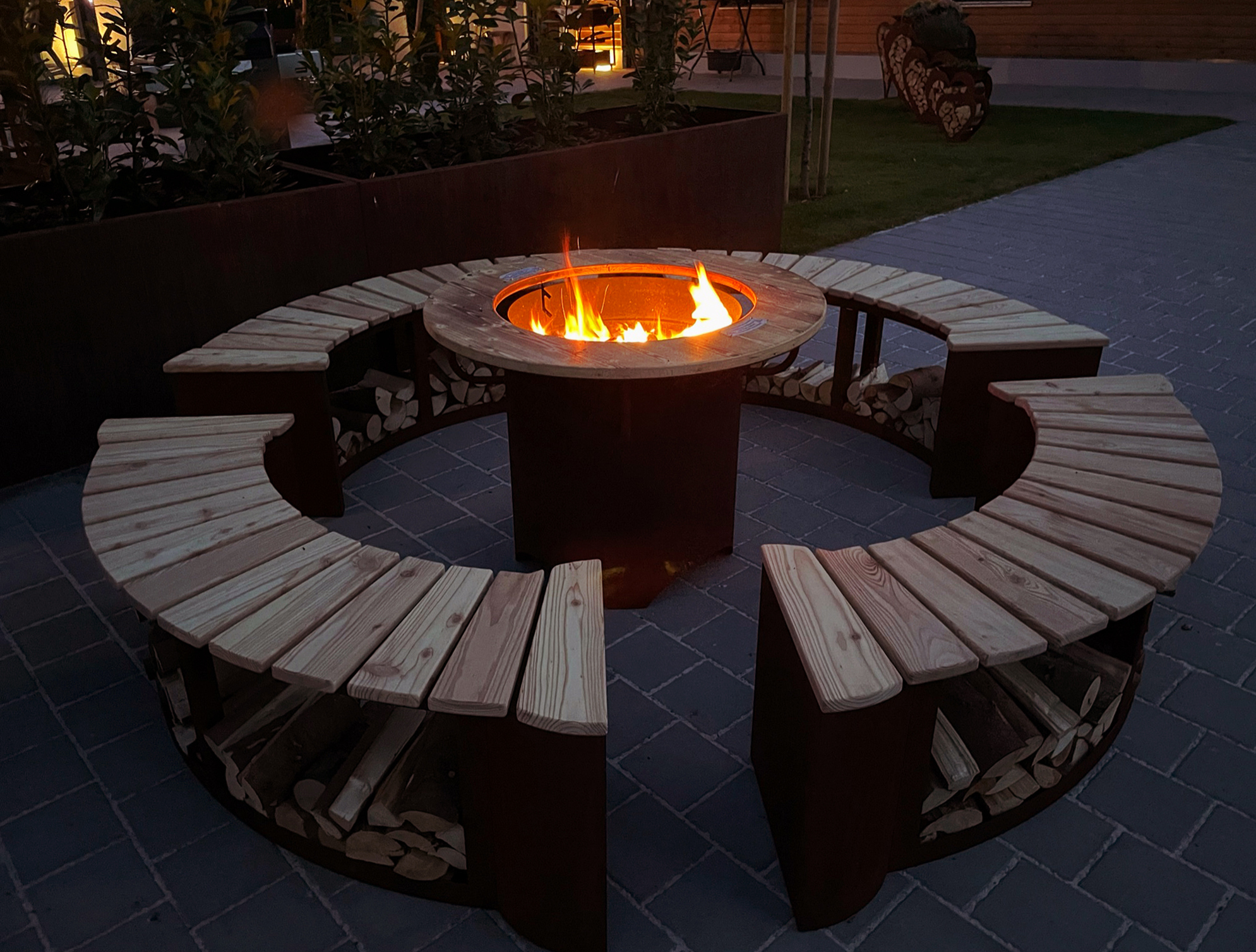 Grill-Feuerstelle Freiburg aus Edelrost mit brennender Feuerstelle und umlaufender Holzablage