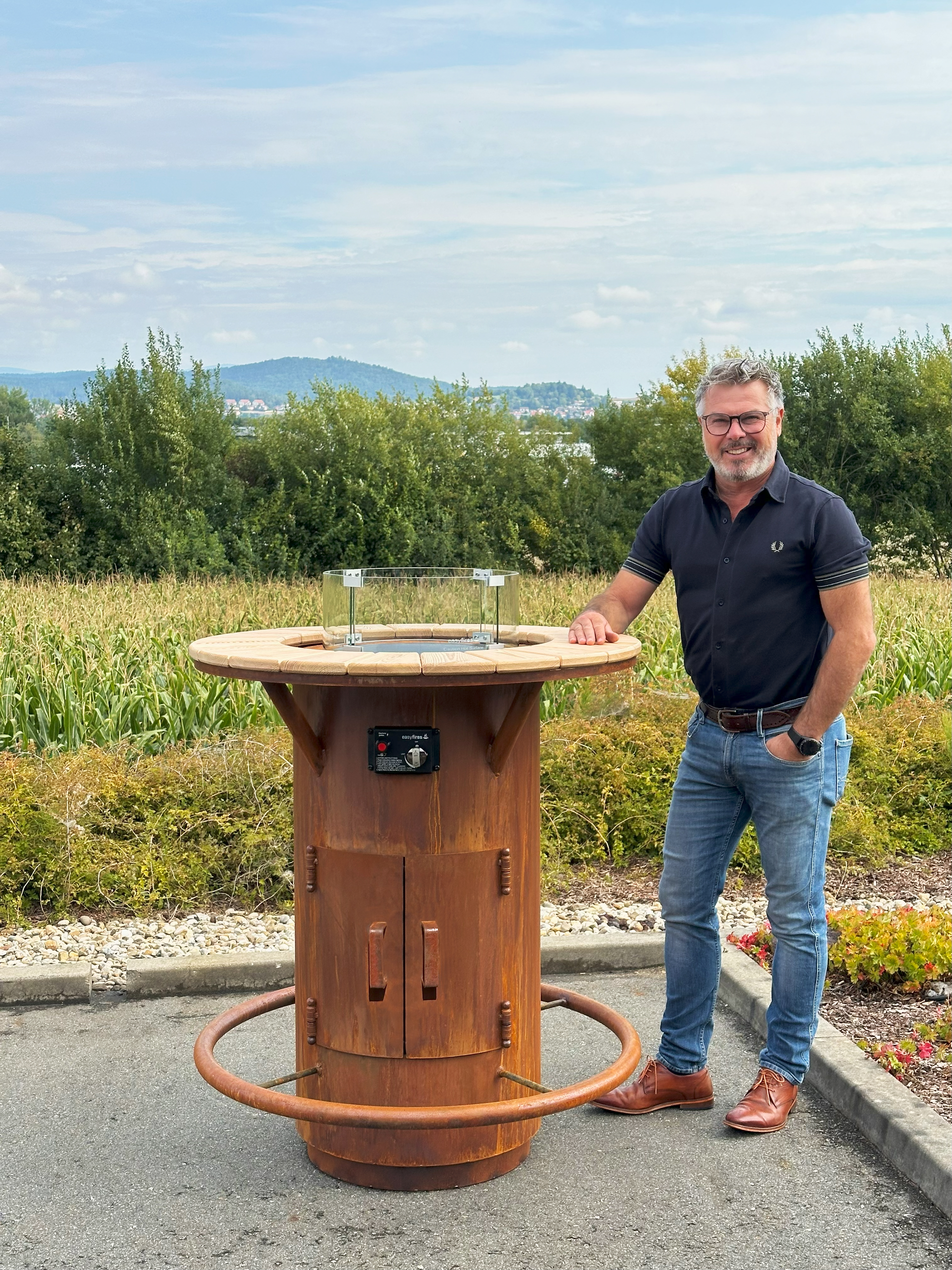 Stehtischofen Ambiente Gasfeuer aus Edelrost mit Person als Größenvergleich im Garten